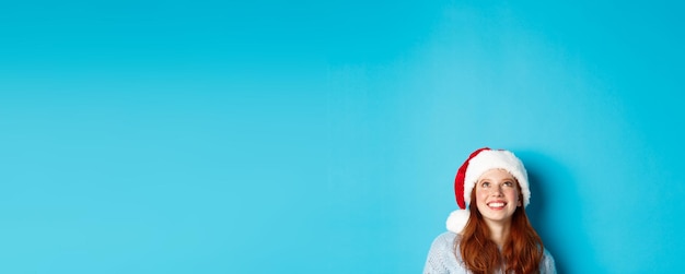 Photo gratuite vacances d'hiver et concept de réveillon de noël tête de jolie fille rousse en bonnet de noel apparaissent du bas