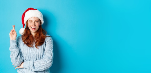 Photo gratuite vacances d'hiver et concept de la veille de noël fille rousse pleine d'espoir en bonnet de noel faisant un vœu sur le cros de noël