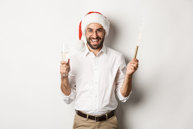 Vacances d'hiver et fête. Bel homme barbu ayant la fête du nouvel an, tenant des étincelles de feu d'artifice et du champagne, portant bonnet de Noel