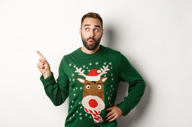 Vacances d'hiver et Noël. L'homme à la curieuse à la promo shopping du Nouvel An, debout dans un pull drôle sur fond blanc.