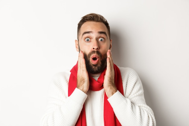 Vacances de Noël. Gros plan sur un barbu surpris disant wow, se tenant la main près du visage, debout sur fond blanc