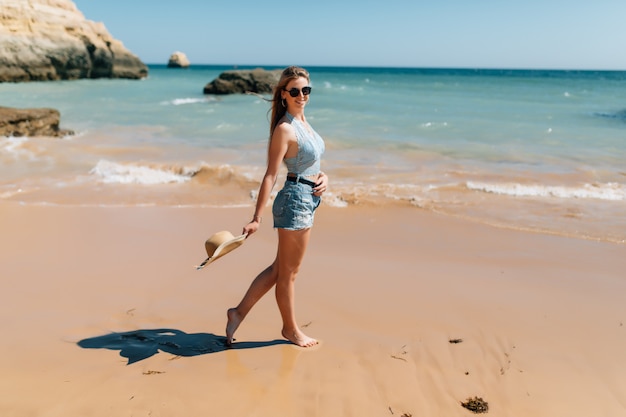 Vacances à la plage. Belle femme en chapeau de soleil bénéficiant d'une parfaite journée ensoleillée marchant sur la plage. Bonheur et félicité.