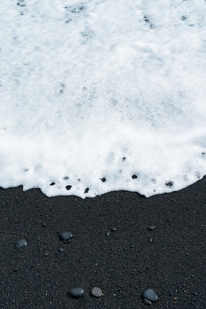 Vague océanique avec mousse blanche roule sur une plage de sable noir avec des galets. Rive sablonneuse volcanique de Tenerife.