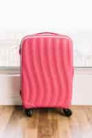 Photo gratuite valise plastique de voyage rose avec roues sur plancher en bois