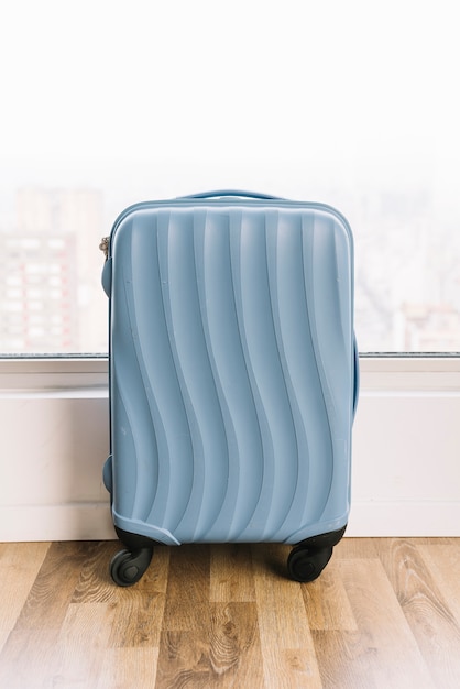 Valise de voyage bleue près de la fenêtre sur plancher en bois