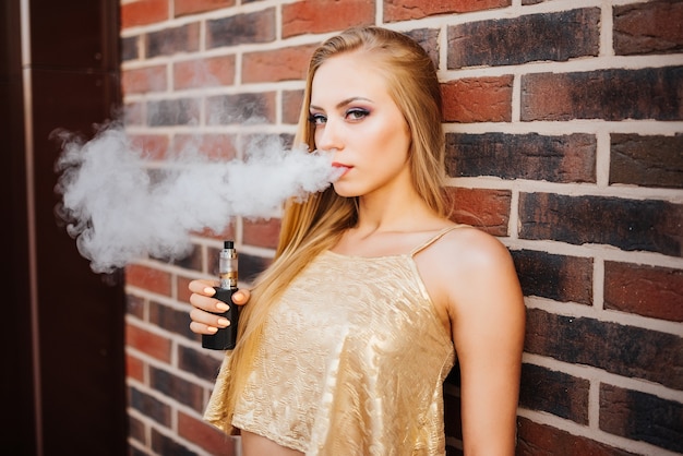 Vaping. Belle jeune femme fumant e-cigarette avec de la fumée à l&#39;extérieur. Concept de vapeur.