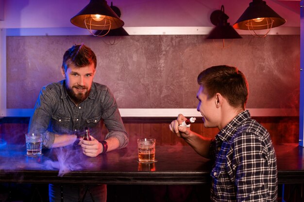 Vaping Homme Tenant Un Mod. Un Nuage De Vapeur Au Vapebar. Deux Hommes Se Reposent Dans Un Bar Et Fument Des Cigarettes électroniques.