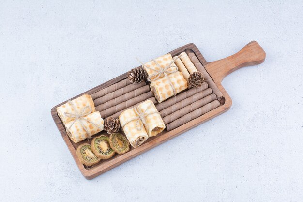 Variété de biscuits et kiwi séchés sur planche de bois.