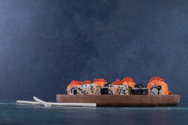 Variété classique de rouleaux de sushi sur planche de bois avec des baguettes.