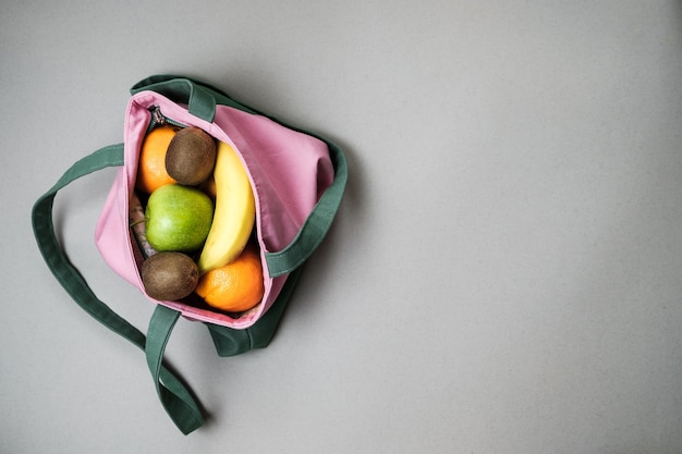 Variété de fruits pamplemousse kiwi banane orange de sac en lin rose sur fond gris vue de dessus avec espace