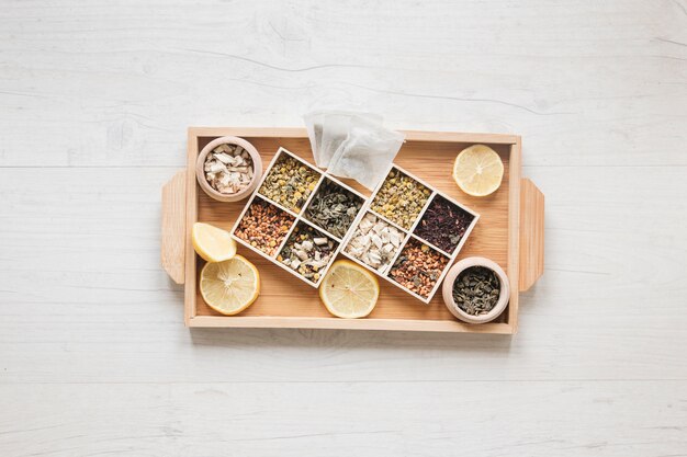 Variété d&#39;herbes et de fleurs de chrysanthème chinois séchées disposées dans un petit récipient sur un plateau en bois