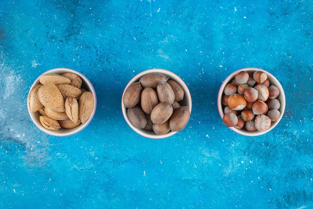 Une variété de noix dans des bols sur la surface bleue