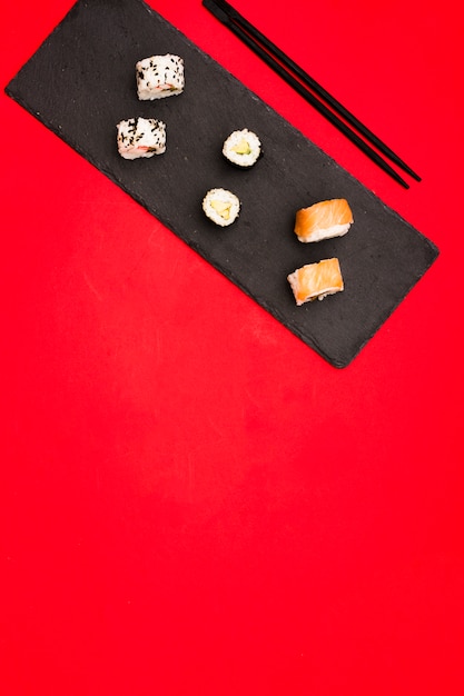 Variété de sushis chauds disposés sur une pierre d&#39;ardoise avec des baguettes sur un fond coloré avec un espace pour le texte