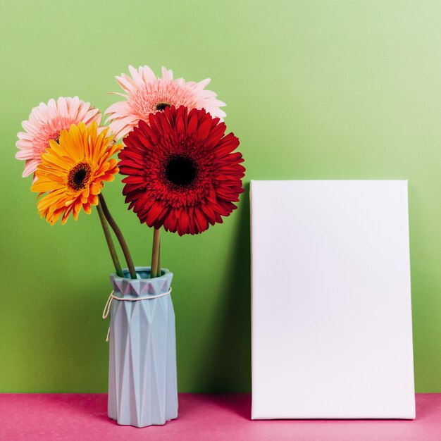 Vase à fleur de gerbera coloré près de la carte vierge sur fond vert