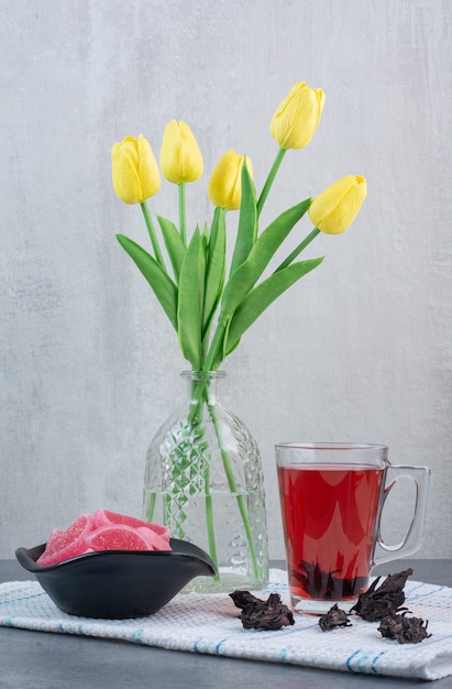 Un vase en verre de fleurs avec une tasse de thé et de marmelade.