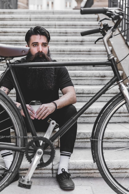 Vélo devant un jeune homme assis sur un escalier tenant une tasse de café à emporter