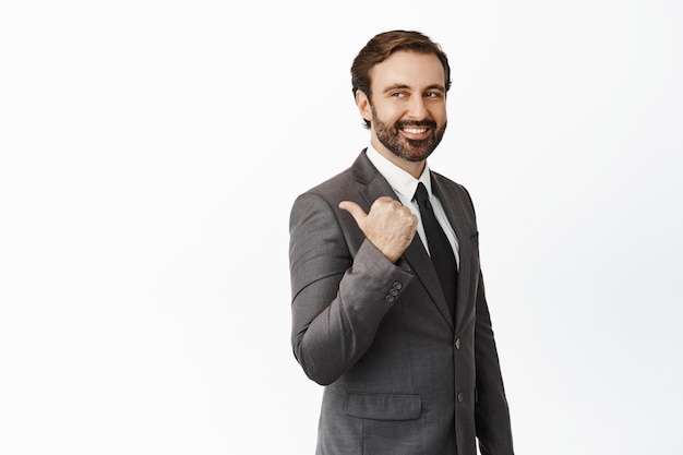 Vendeur charismatique en costume pointant et regardant à gauche sur la bannière de l'entreprise signe montrant la publicité debout sur fond blanc