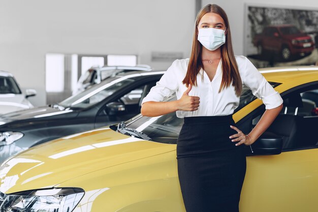 Vendeur de voiture femme debout près de la nouvelle voiture portant un masque protecteur