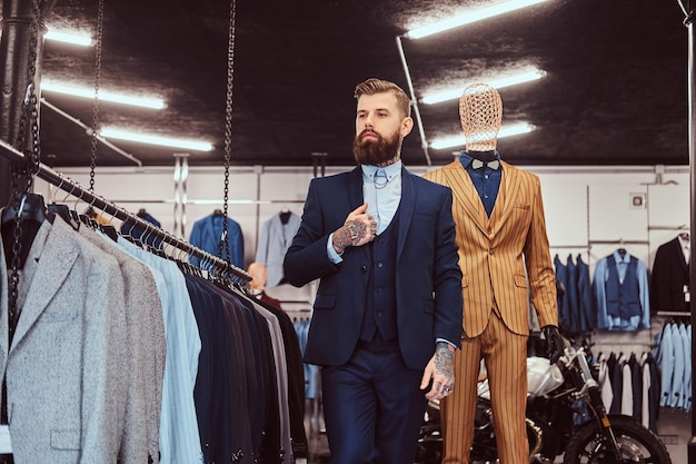 Vendeuse barbue élégamment vêtue, debout près d'un mannequin dans un magasin de vêtements pour hommes.