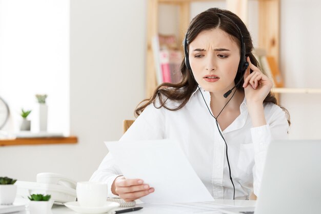 Vendeuse bien habillée sérieuse parlant au téléphone au bureau derrière son bureau et espace de copie de l'ordinateur portable