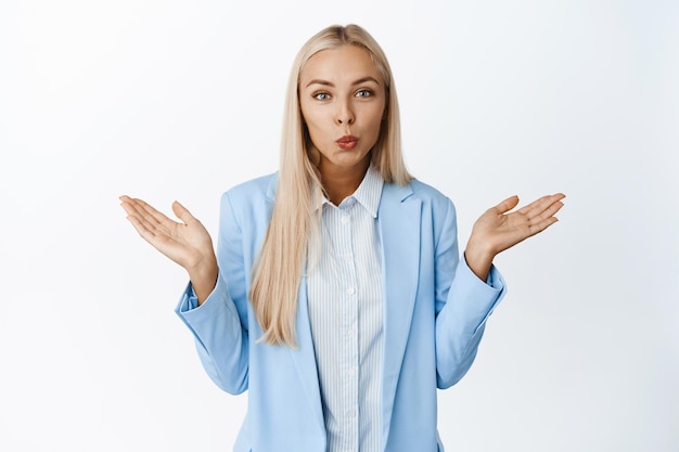 Vendeuse blonde mignonne haussant les épaules à la moindre idée ne sais pas ne peut pas comprendre debout en costume bleu sur fond blanc