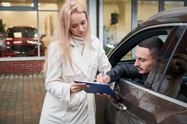 Photo gratuite vendeuse demandant à signer des documents d'achat de voiture