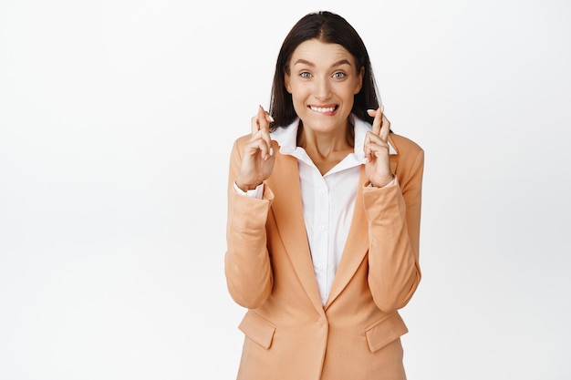 Vendeuse de directeur de bureau pleine d'espoir priant en faisant un vœu et croisant les doigts pour la bonne chance mordant la lèvre excitée debout en costume sur fond blanc