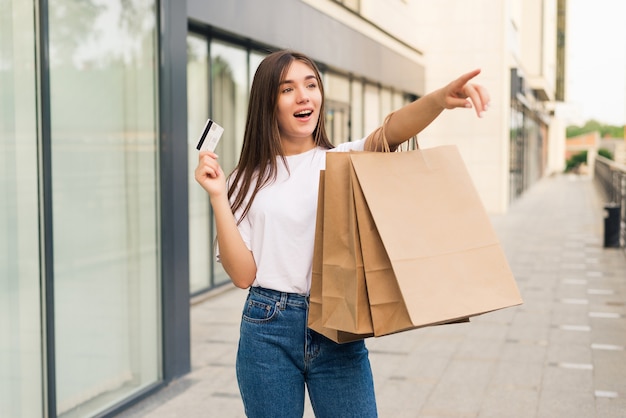 Vente, shopping, tourisme et concept de gens heureux - belle femme avec des sacs à provisions et carte de crédit dans les mains dans une rue