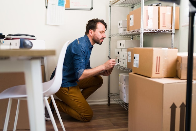 Vérifier que tous les colis sont en ordre. Bel homme écrivant sur un presse-papiers les informations des clients pour expédier leurs achats en ligne