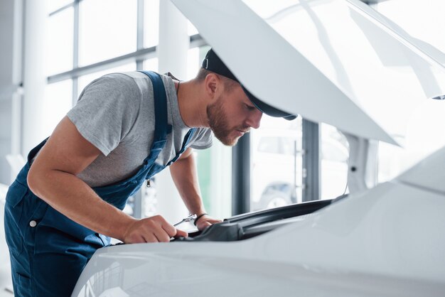 Vérifier si les détails sont corrects. Homme en uniforme bleu et chapeau noir réparant une automobile endommagée