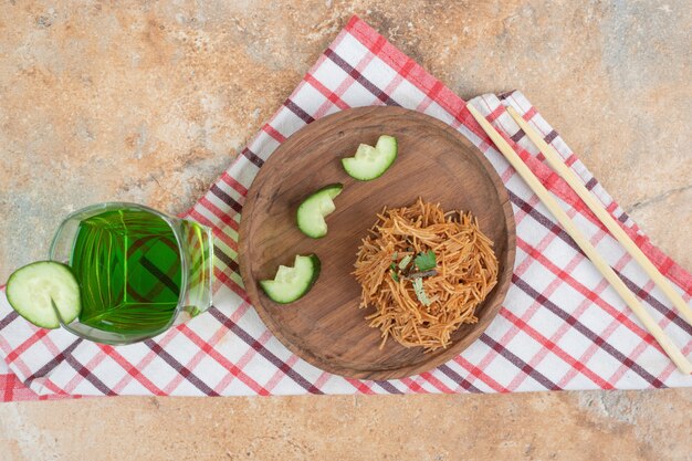 Vermicelles frits avec des tranches de concombre sur une plaque en bois et un verre de jus