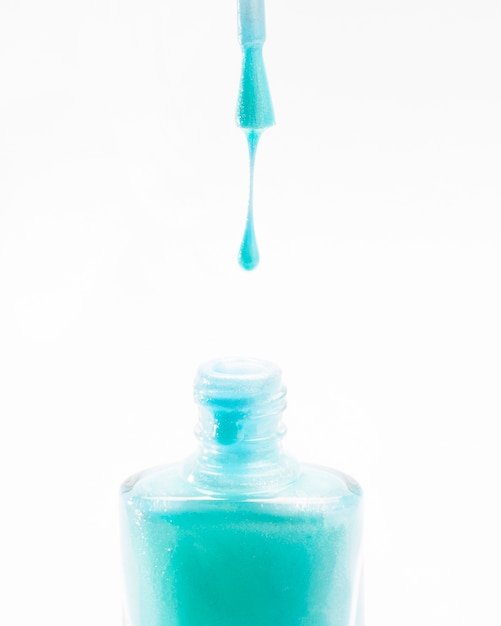 Vernis à ongles turquoise dégoulinant de la brosse dans la bouteille