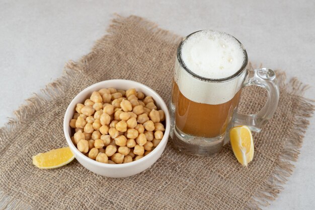 Verre de bière avec bol de pois et tranches de citron sur toile de jute