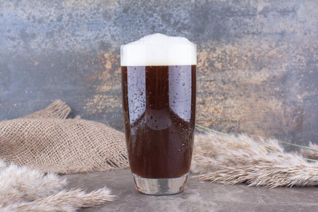 Verre de bière brune avec des épis de blé sur une table en marbre. photo de haute qualité