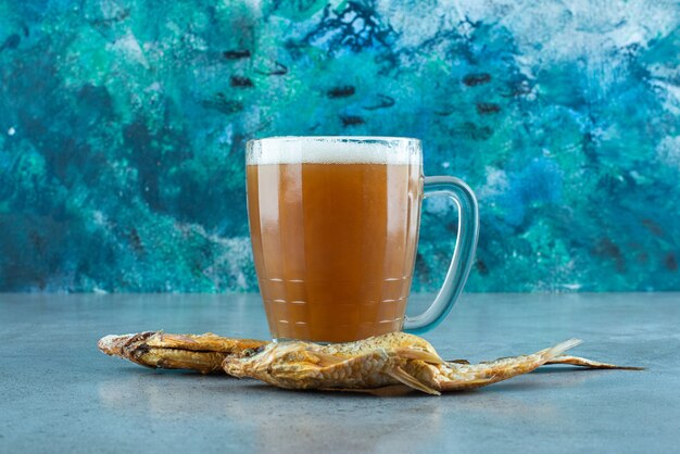 Un verre de bière à côté de poissons, sur la table bleue.