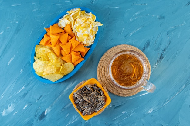 Verre de bière sur un dessous de plat à côté de diverses puces dans une assiette en bois , sur la surface bleue.