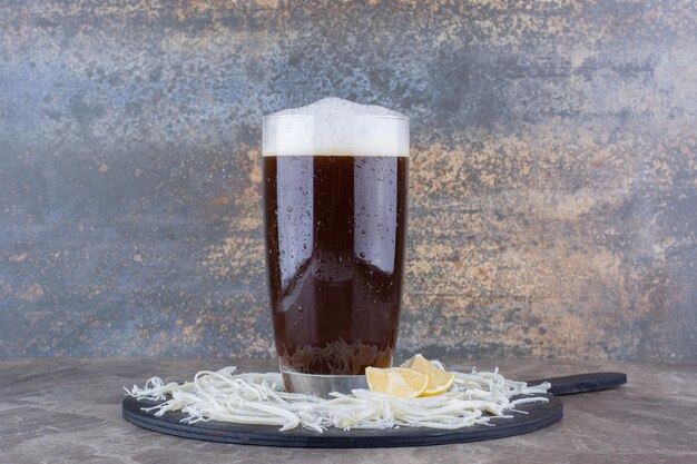 Verre de bière avec du fromage et des citrons sur une planche sombre. photo de haute qualité
