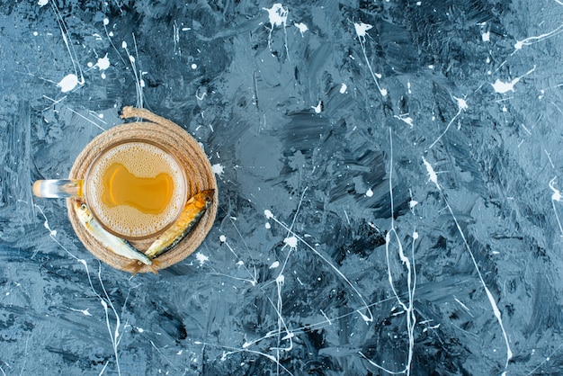 Un verre de bière et de poisson sur un dessous de plat, sur le fond bleu.