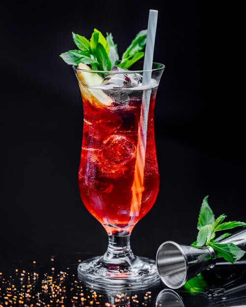 Un verre de boisson rouge avec des feuilles de menthe et une pipe.