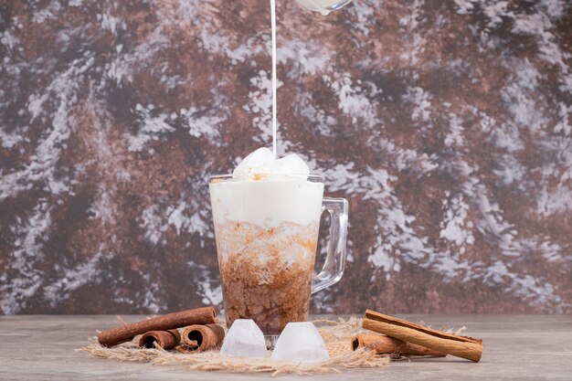 Verre avec boisson savoureuse et cannelle sur table en marbre.