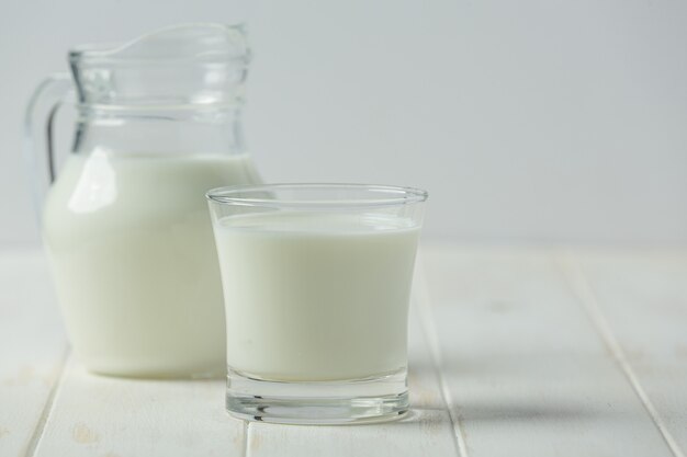Verre et bouteille de lait sur surface de bois blanc
