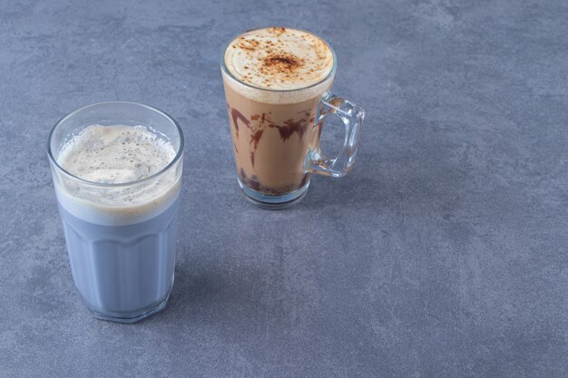 Un verre de café bleu à côté d'un cappuccino au chocolat, sur la table bleue.