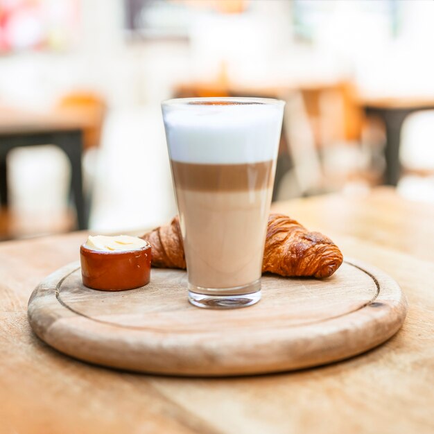 Verre à café Cappuccino avec croissant sur un plateau en bois