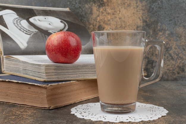 Un verre de café chaud avec une pomme rouge et des livres sur une surface en marbre.