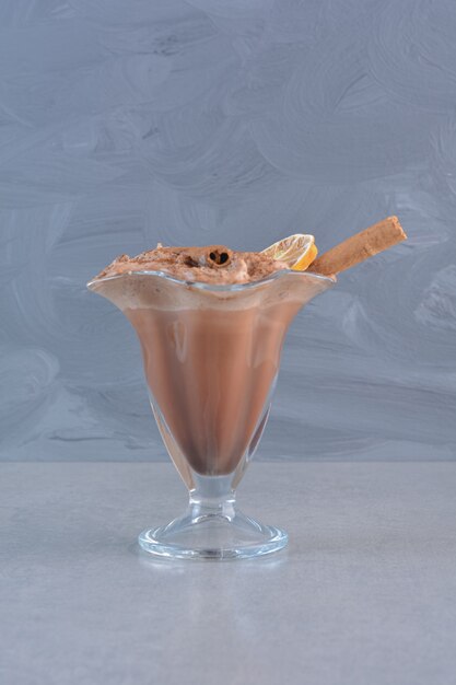 Un verre de chocolat chaud décoré de bâtons de cannelle sur fond de pierre.