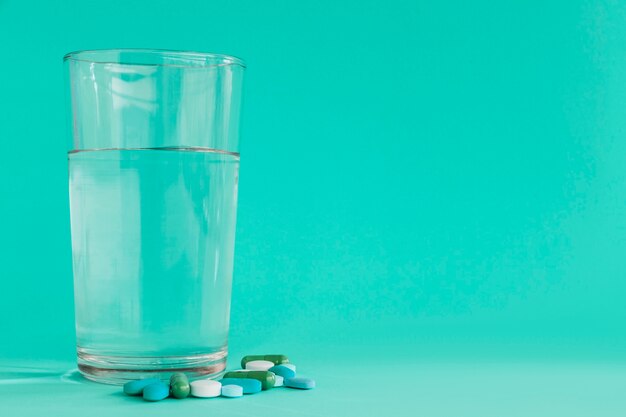 Verre clair d&#39;eau avec des pilules sur fond turquoise