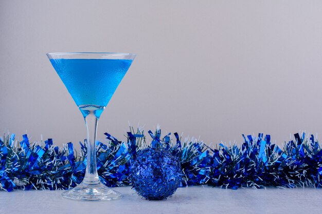 Verre à cocktail à côté de décorations de Noël bleu sur fond blanc.