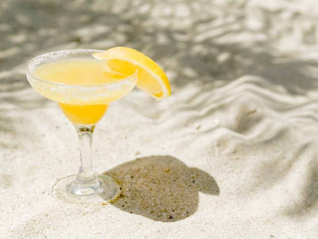 Photo gratuite verre de cocktail jaune avec une tranche de citron posée sur le sable
