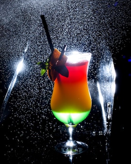 Un verre de cocktail ombre avec du jus vert et orange sur fond sombre avec de la lumière