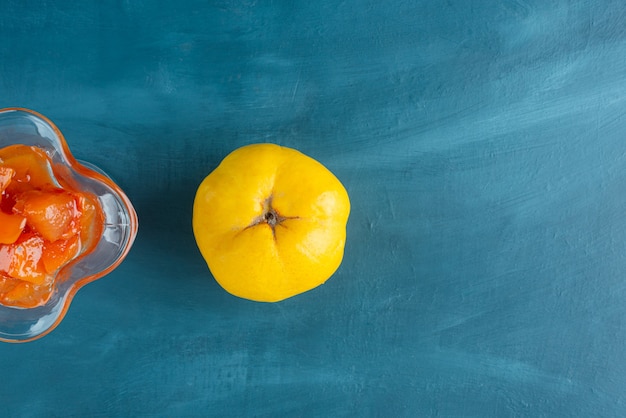 Verre de confiture de coings et fruits de coings sur une surface bleue.